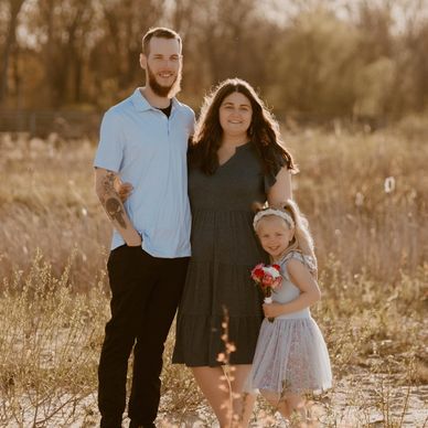 A happy family of three posing outdoors in a sunlit field.