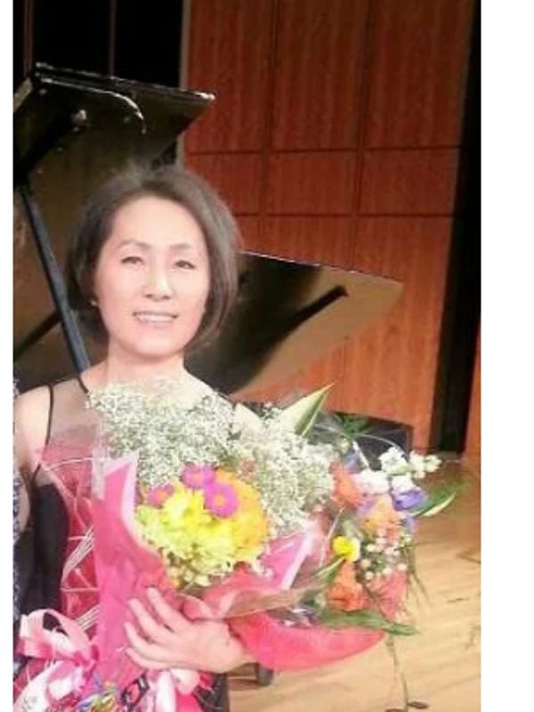 Woman holding colorful flower bouquets on a stage with a piano.