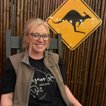 Smiling woman in glasses with kangaroo-themed clothing and sign.
