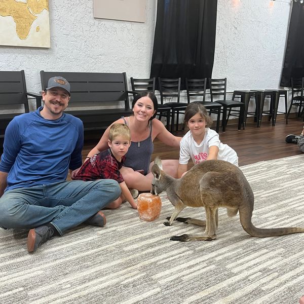 Family sitting on floor with a kangaroo indoors.