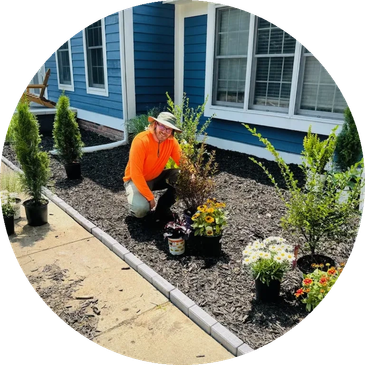 Person gardening in front of a blue house with various plants ready for planting.