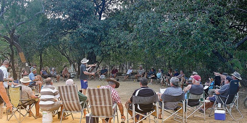 Group outdoor meeting with people seated in a circle under trees.