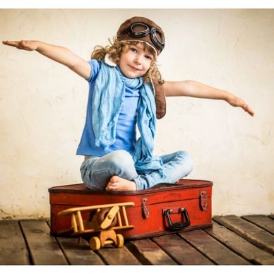 Child playing pilot, sitting on suitcase with toy airplane.