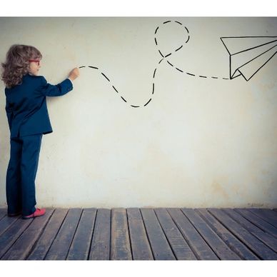 Child in suit drawing flight path of paper airplane on wall.