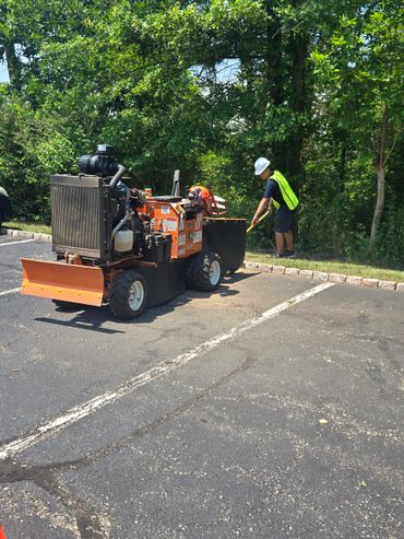 Worker with safety vest and helmet operating machinery near trees.