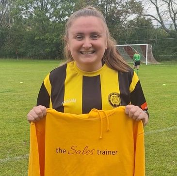 Young woman in a black and yellow sports jersey holding a yellow hoodie with text.