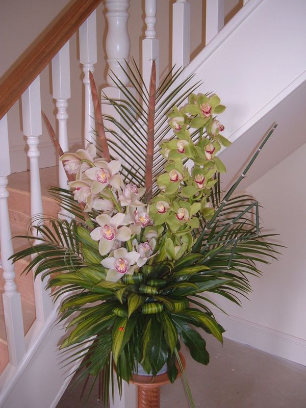 modern pedestal arrangement of cymbidium orchids and palm leaves