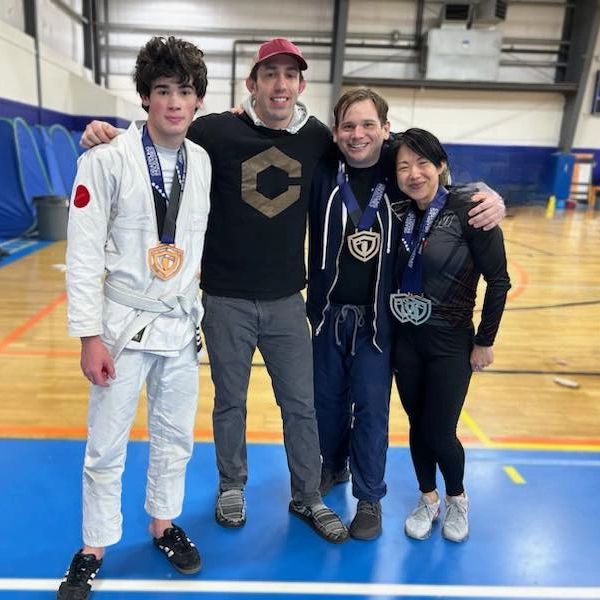three team members and a coach stand together smiling with a gold and three silver metals in a gym