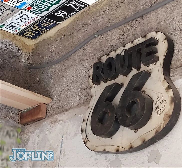 Vintage Route 66 sign mounted on a textured wall with nostalgic license plates above.