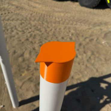 Bright orange cap on a white pole in a sandy area.