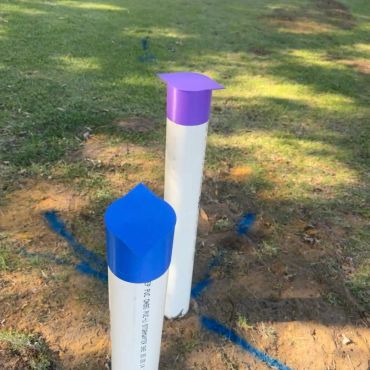 Two white PVC pipes with blue and purple caps on a grassy patch.