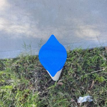 Blue-capped white pole in grass near sidewalk.