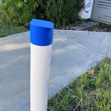 White post with blue top near grass and sidewalk.