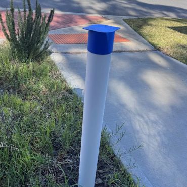 White pole with blue cap in grass near sidewalk.