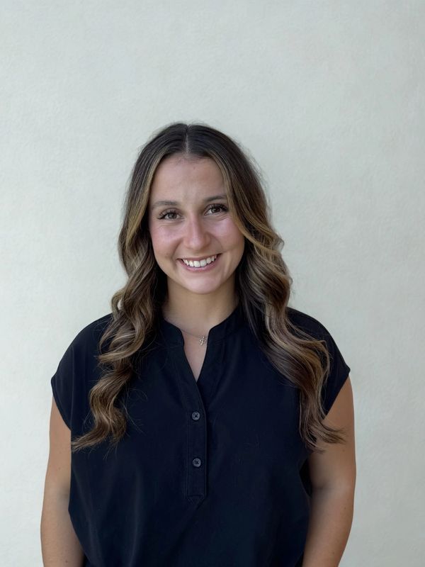 Smiling woman with wavy hair wearing a black blouse against a plain background.