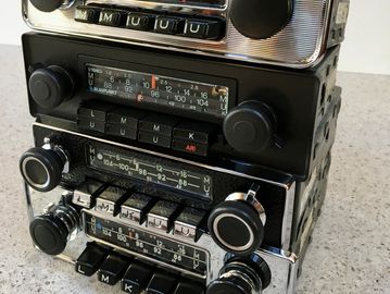 Stack of vintage car radios with tuning knobs and buttons.