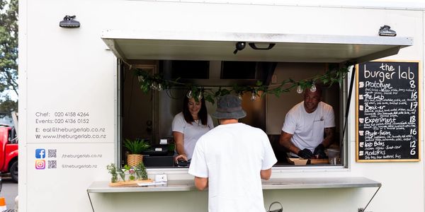 Customer ordering at The Burger Lab food truck with menu and staff visible.