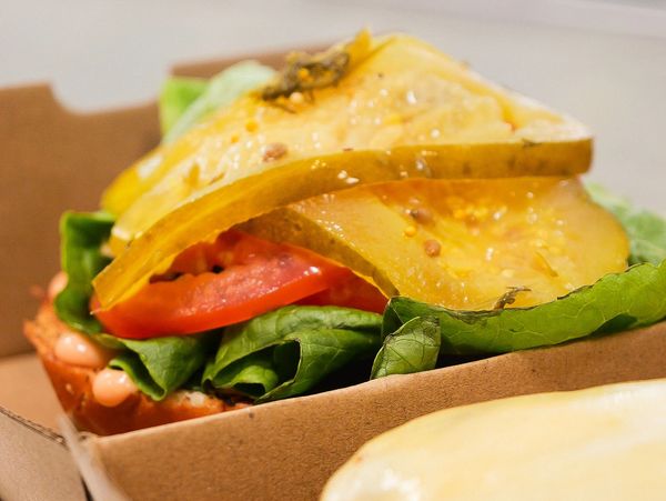 Close-up of a fresh sandwich with pickles, lettuce, tomato, and melted cheese.