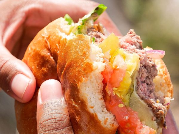 Close-up of a hand holding a partially eaten cheeseburger with lettuce and tomato.