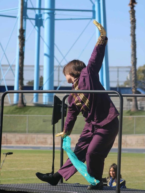 Person in purple costume and gold gloves performing a dance move outdoors.