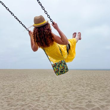 Woman in yellow dress swinging on a beach swing under an overcast sky.