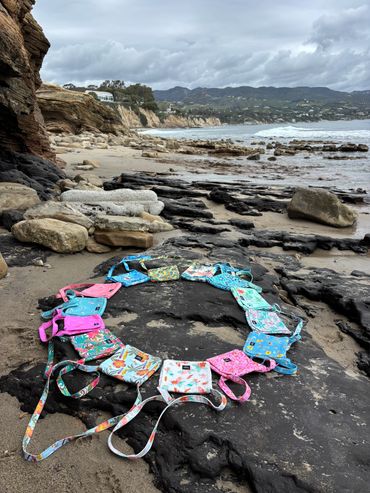 Colorful bags arranged in a circle on rocky beach under a cloudy sky.