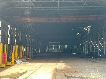 Abandoned industrial warehouse with yellow barriers and sunlight patches on the floor.