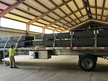 Worker inspecting metal beams loaded on a flatbed truck inside a warehouse.