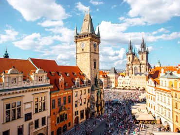 Historic city square with clock tower and Gothic church under a bright sky.
