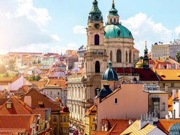 Sunlit cityscape with historic buildings and domed church towers.
