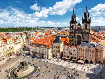 Historic town square with Gothic church and vibrant rooftops under a blue sky.