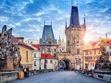 Historic stone bridge with statues and towers under a bright sky at sunrise.
