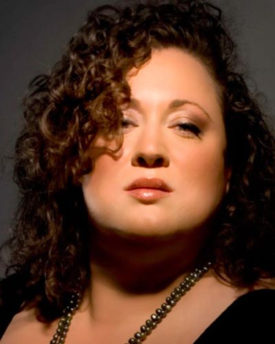 Confident woman with curly hair and dramatic makeup.