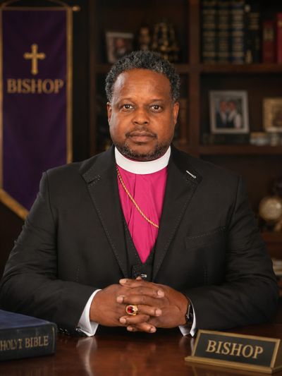 A bishop in formal attire sitting at a desk with religious items.