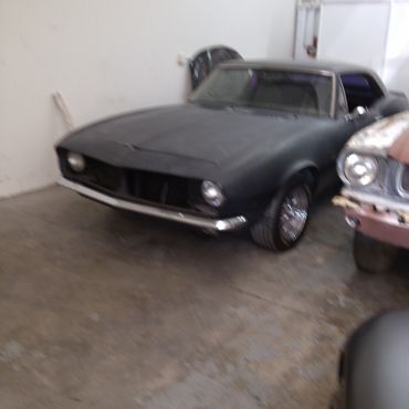 A black vintage car parked indoors next to another old car.