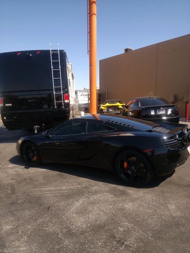 A sleek black sports car parked in a lot with other vehicles under clear blue sky.