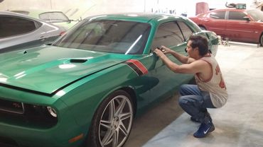 Man installing decals on a green Dodge Challenger in a garage.