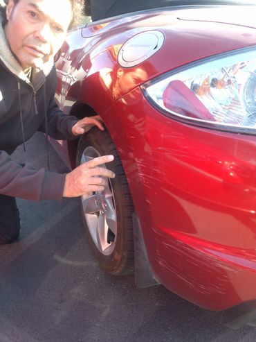 Man inspecting scratches on a red car's front tire and fender.
