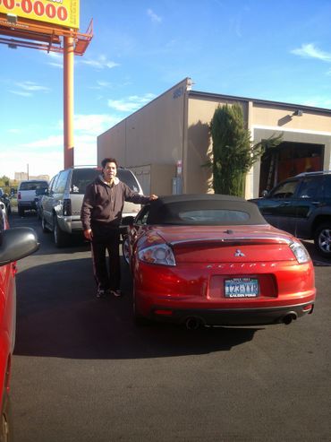 A man stands beside a red Mitsubishi Eclipse convertible in a parking lot.