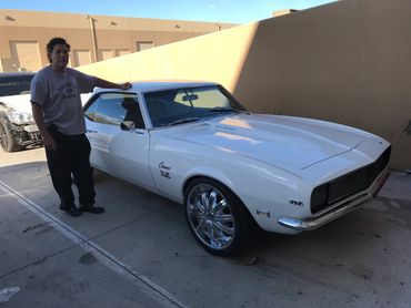 Man standing beside a white classic Chevrolet Camaro SS with shiny rims.