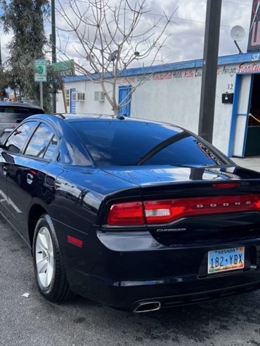 Black Dodge Charger parked on a city street near an upholstery shop.