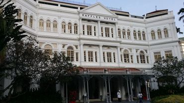 The historic white facade of Raffles Hotel with lush greenery in front.