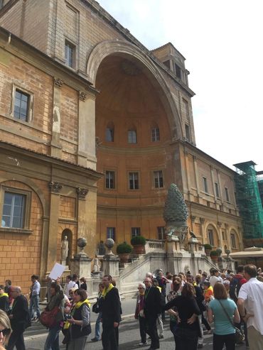 Tourists gather outside a historic building with a large arched niche and stone sculptures.
