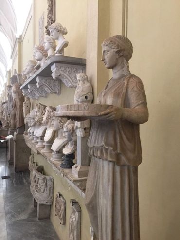 Ancient marble statues and busts displayed in a museum corridor.