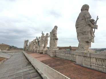 A row of large stone statues on a rooftop against a cloudy sky.