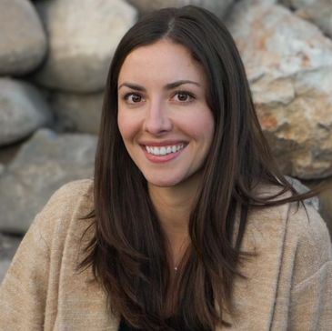 Smiling woman with long dark hair in a cozy beige sweater.