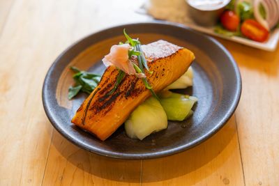 A plate of misoyaki salmon served on a bed of bok choy and topped with green onions and ginger.