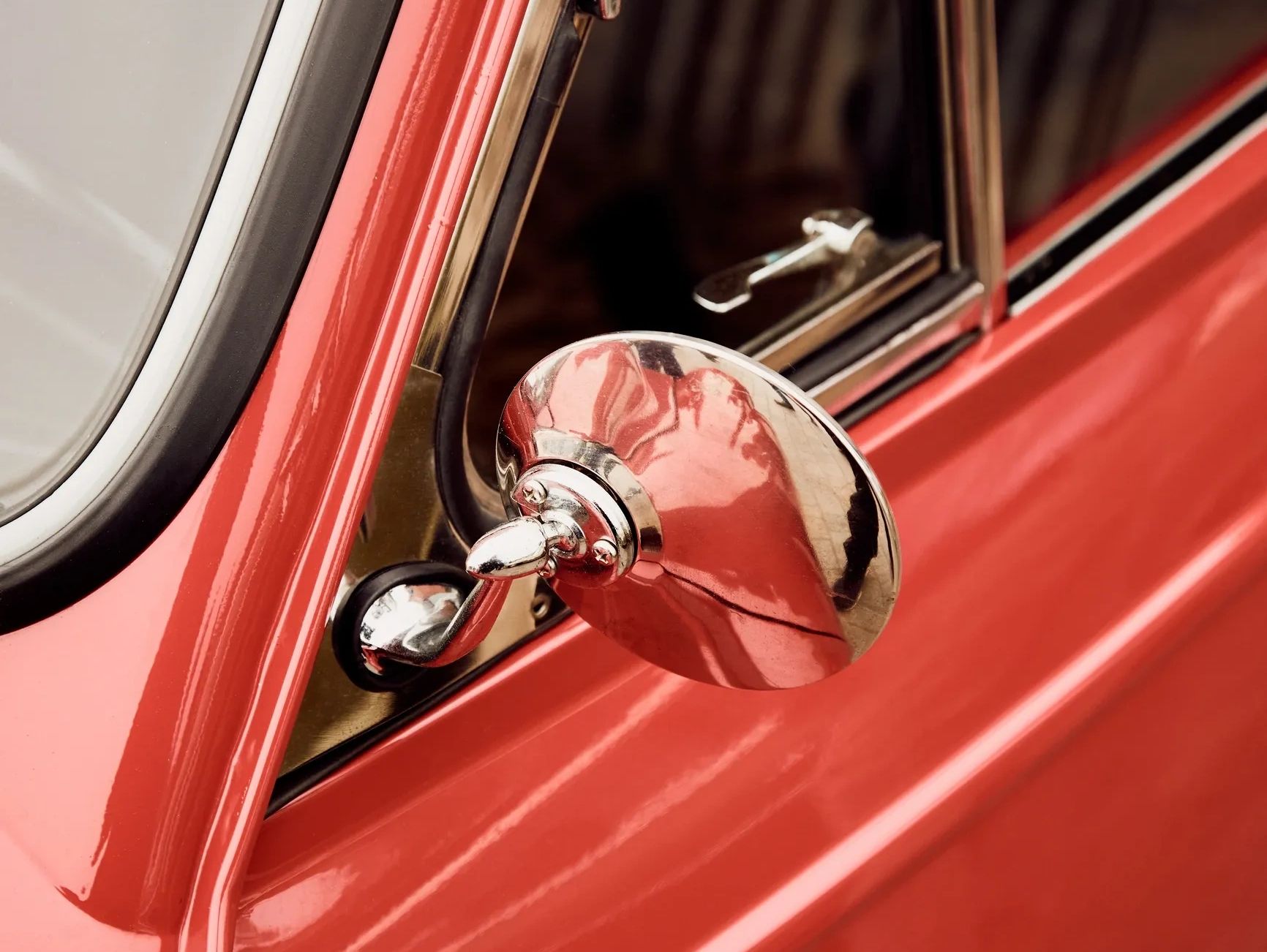 Close-up of a red vintage car's chrome side mirror and window.
