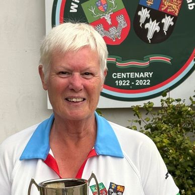 Older woman holding a trophy with a centenary sign behind her.