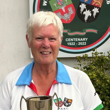 Older woman holding a trophy with a centenary sign behind her.